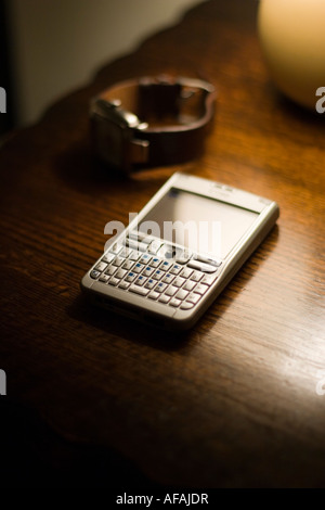 Ein Nokia E61 Smartphone auf eine polierte antiker Tisch mit einer Herrenuhr mit braunem Lederarmband mit einer kleinen Lampe beleuchtet Stockfoto