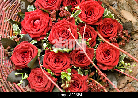 Nahaufnahme eines wunderschönen Blumenarrangements aus roten Rosen mit grünen Blättern und dekorativen Zweigen auf einem rustikalen Hintergrund. Stockfoto