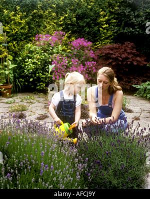 Kleinkind alt mit ihrer Mutter mit einer Gießkanne, Lavendel Pflanzen im Garten Wasser Stockfoto