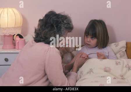 Mutter ihre Tochter s Hand haltend, wie sie im Bett liegt Stockfoto