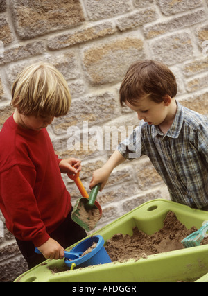 Jungen spielen mit einem Kunststoff Spaten und Containern in einem Sand Tablett Stockfoto