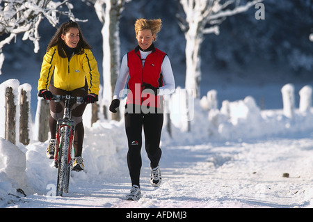 Frau mit dem Fahrrad neben Jogger auf einer verschneiten Straße, Ramsau, Steiermark, Austria, Europe Stockfoto