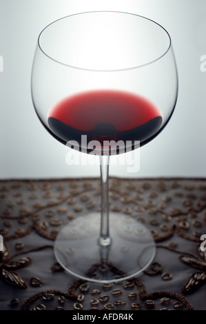 Weinglas mit Rotwein auf einer Perlen Tischdecke teilweise gefüllt. Der Hintergrund ist hell erleuchtet. Stockfoto
