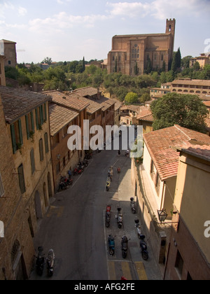 Schmale Straße mit Wohnhäusern und-Roller und San Domenico in Siena Italien Rücken Stockfoto