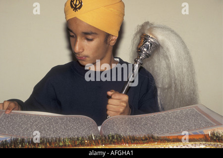 Ein Sikh-Junge, der den Guru Granth Sahib mit dem traditionellen Chauri- oder Ochsenschwanz-Fächer liest, verwendete, um Fliegen von den heiligen Texten zu halten, die in den Gurdwara gehalten werden. Stockfoto