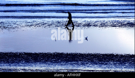 In den Wasserbecken der Sussex-Küste spiegelt sich in der Abenddämmerung ein Fischer, der Köder sammelt, während er im verblassenden Licht am Strand spazieren geht. Stockfoto