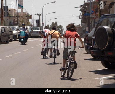 drei Kinder auf dem Fahrrad Reiten vom Betrachter und ein Mann auf einem Roller fahren in Richtung Betrachter auf einer Straße auf Sizilien in Italien Stockfoto