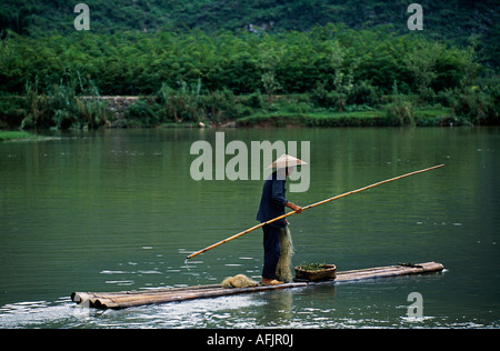 Yulong Fluss, Nr Yangshuo, Guangxi Provinz. Ein Fischer Polen seine Bambus-Floß auf dem ruhigen Fluss Stockfoto