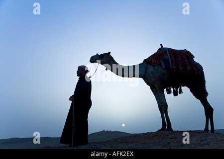 Ein Beduine führt sein Kamel an der Spitze einer Düne bei Sonnenuntergang, Gizeh, Ägypten. (MR). Stockfoto