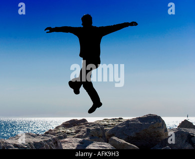 Silhouette der junge Mann springt auf Felsen am Seeufer Stockfoto