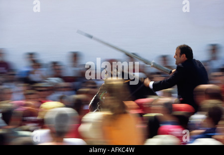 Ein Reiter auf dem Pferd beschleunigt durch die Menge, die ein Ziel mit einer Lanze zu schlagen versucht. Stockfoto