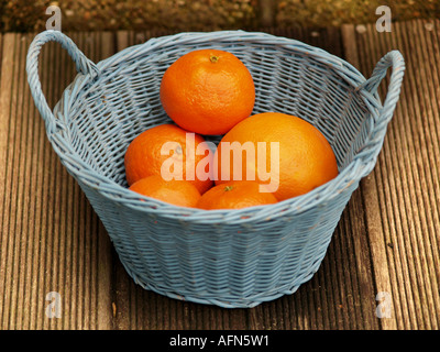 einige Orangen in blassen blauen Korb auf hölzernen Tischplatte im freien Stockfoto