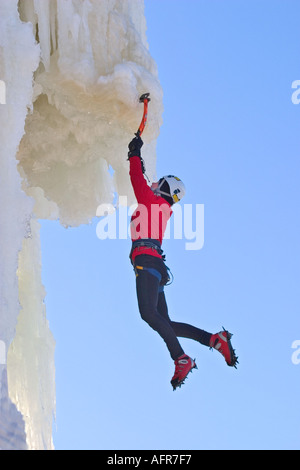 Kaukasische weibliche Eiskletterer Klettern auf Eiswand mit Eispickel und Steigeisen . Hängen an der Eispickel am Überhang, Finnland Stockfoto