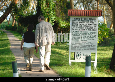 Paar vorbeigehen Schild Warnung vor der Gefahr von Wildtieren auf dem Gelände des Lake Naivasha Club Kenia in Ostafrika Stockfoto