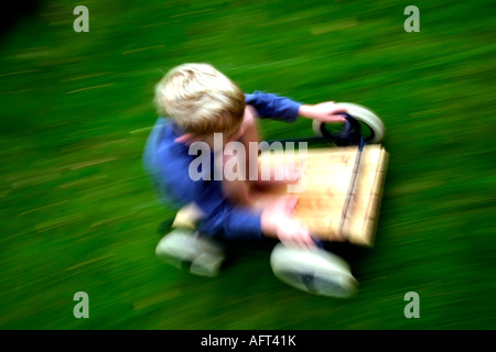 6 Jahre alter Junge Reiten eine hausgemachte Buggy oder Go-kart mit Geschwindigkeit auf Rasen Stockfoto