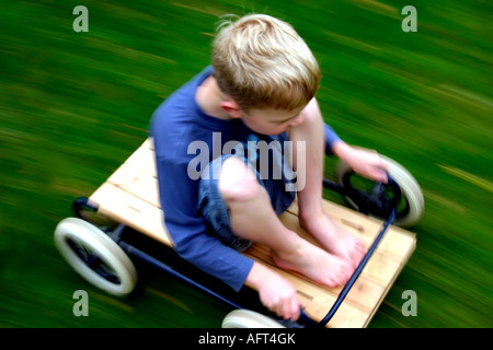6 Jahre alter Junge Reiten eine hausgemachte Buggy oder Go-kart mit Geschwindigkeit auf Rasen Stockfoto