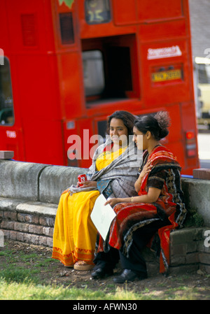 Asiatische junge Frauen in Saris sitzen auf einer Bank Bangladeshi Gemeinschaft Ost London Bus im Hintergrund 1990er UK HOMER SYKES Stockfoto