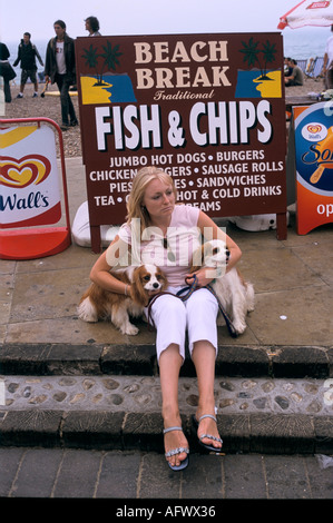 Eine Frau mit ihren Hunden, die vor einem Schild mit einem Fish and Chips Shop sitzt. Brighton East Sussex England. Um die 1995 1990er Jahre britischer HOMER SYKES Stockfoto