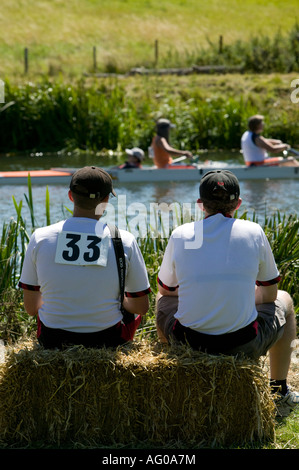 Zwei Männer tragen schwarze Baseball-Kappen sitzen auf Heu Ballen beobachten Menschen Ruderboot Fluss Stour Sudbury Suffolk England Stockfoto