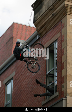 Mountain Bike Radfahrer Abseilen eine Mauer mit einem Beinpaar ragen aus einem Büro-Fenster Edinburgh Schottland Stockfoto