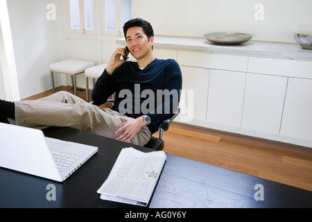 Asiatische Männer sprechen auf seinem Handy während der Arbeit an seinem Laptop-Computer in seinem Haus-Büro Stockfoto