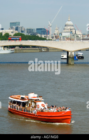 Ein Ausflugsschiff mit Touristen hat soeben Waterloo Bridge mit einem roten Bus und St Pauls Cathederal im Hintergrund. Stockfoto