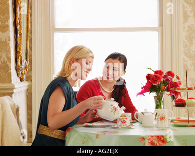 Zwei junge Frauen sitzen am Esstisch, Tee gießen Stockfoto
