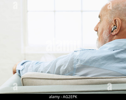 Mann mittleren Alters tragen Kopfhörer, auf Sofa sitzen und auf die Seite, Ansicht von hinten Stockfoto