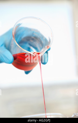 Wissenschaftler, die rote Flüssigkeit aus Becher, Nahaufnahme der Hand gießen Stockfoto