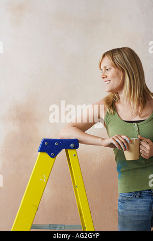 Lächelnde Frau stützte sich auf die Trittleiter, mit Becher Stockfoto