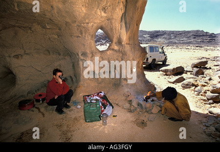 Algerien in der Nähe von Tamanrasset Tourist zu Mittag mit Mann der Tuareg Stamm sitzen am Kamin Stockfoto