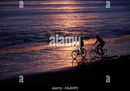 Ein paar fährt Fahrräder am Strand in Kalifornien bei Sonnenuntergang. Stockfoto