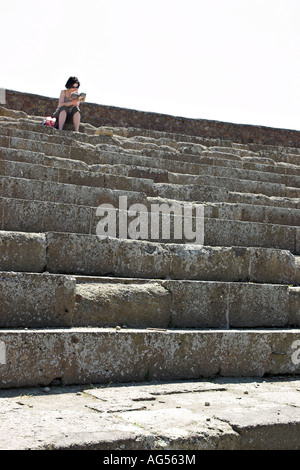 Den Guide zu tun sitzt eine junge Frau allein hoch bis auf das alte Amphitheater, den Leitfaden für die archäologische Stätte zu studieren Stockfoto