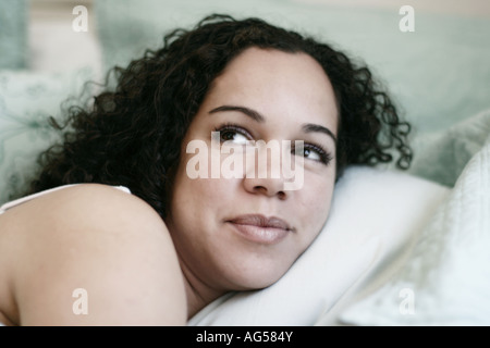 Mädchen Gesicht Schulter und Kissen dunkle lockige Haare braune Augen Aqua Hintergrund hautnah Stockfoto