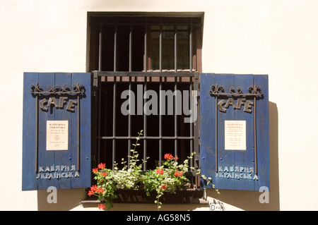 Blaue Fensterläden eines ukrainischen Cafés in der Kanoniczna Straße in der Altstadt von Krakau, Polen, mit Metallschildern, Menüs und roten Fensterblumen. Stockfoto