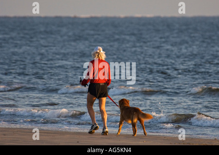 Mann mit Hund an der Leine, Joggen am Strand neben Ozean vor Sonnenuntergang Sullivans Island South Carolina Stockfoto