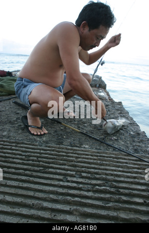 Ein Mann Prämiensystem auszuklinken einen Fisch fing er beim Angeln vor Sonnenaufgang am Ende der Betonpfeiler am Waikiki Beach auf Hawaii Stockfoto