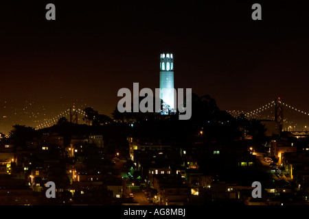 Coit Tower beleuchtet in der Nacht mit der Bay Bridge im Hintergrund und die Häuser Straßen des Telegraph Hill im Vordergrund Stockfoto