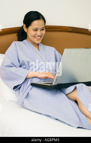 Junge Chinesin auf Bett im Hotelzimmer arbeiten am Laptop Computer Bangkok Thailand Stockfoto
