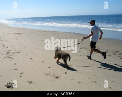 Mann mit einem Hund an einem Strand läuft Stockfoto