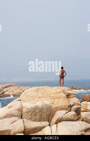 Mann steht auf Felsen direkt am Meer Stockfoto