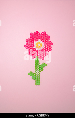 Rosa Kunststoff Blume aus Perler Perlen auf einem rosa Hintergrund hergestellt. Stockfoto