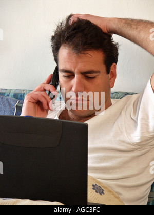Junger Mann tragen T-shirt erstreckt sich auf Bett mit Blick auf tragbaren Computer-Bildschirm auf der Thoughtfu Suche Handy reden Stockfoto