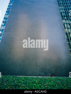 ein Mann sitzt mit seinem Motorrad gegen die Basis eines riesigen Wolkenkratzer-Gebäudes Stockfoto