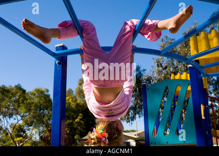 weibliches Kind kopfüber auf Spielplatz, Klettergerüst, vor einem tiefblauen Himmel Stockfoto