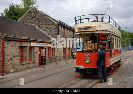 Eine offene überstieg High St Straßenbahn-Haltestellen auf den gepflasterten Straßen in Crich Tramway Museum und ein Fußgänger auf der Strecke im Gespräch mit der straßenbahnfahrer. Stockfoto