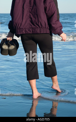 Frau im Mantel geht im Wasser halten Schuhe bei Hunting Island Beach SC im Herbst USA Stockfoto