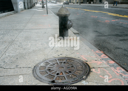 Dampf steigt von Dpw-Einsteigeloch-Abdeckung auf Bürgersteig mit alten altmodischen Hydranten New York City New York USA Stockfoto