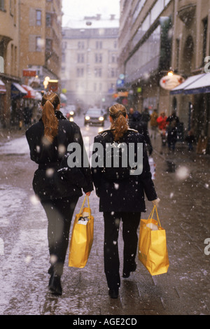 Zwei Frauen mit gelben Weihnachten Einkaufstüten zu Fuß durch Licht Schnee in Stockholm Stockfoto