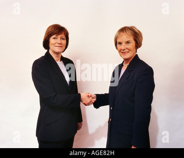 Zwei Geschäftsfrauen schütteln sich die Hände sind beide tragen Anzüge und schaut in die Kamera Stockfoto